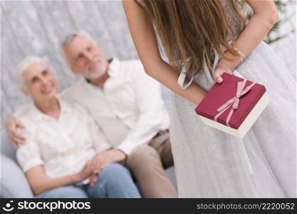 little girl hiding gift her back front her grandparents sitting sofa