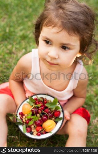 Little girl holds a bowl with summer fruits