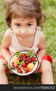 Little girl holds a bowl with summer fruits. Summer fruits