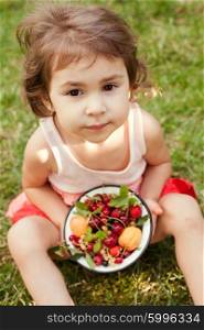 Little girl holds a bowl with summer fruits. Summer fruits