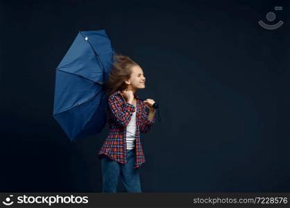 Little girl holds an umbrella in studio, wind effect, powerful airflow. Children with developing hairs, kids isolated on dark background, child emotion. Little girl holds an umbrella, wind effect