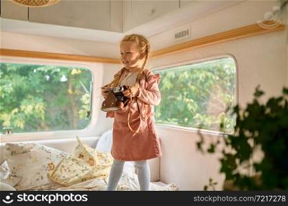 Little girl holds camera in motorhome, summer camping. Family with children travel in camp car, trailer interior on background. Campsite adventure, travelling lifestyle, funny kid in rv car. Little girl holds camera in motorhome, camping