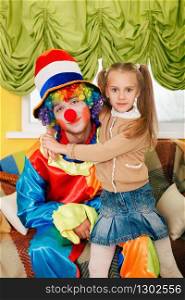 Little girl hugging a cheerful clown with rainbow coloured hair.