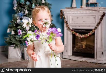 Little girl in a celebratory dress plays near the Christmas tree