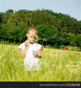 Little girl in a field making soap bubbles and having fun with it