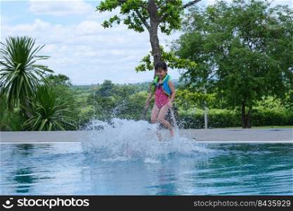 Little girl in a life vest jumps into an outdoor swimming pool. Cute little girl playing in the pool on a sunny day. Summer lifestyle concept.