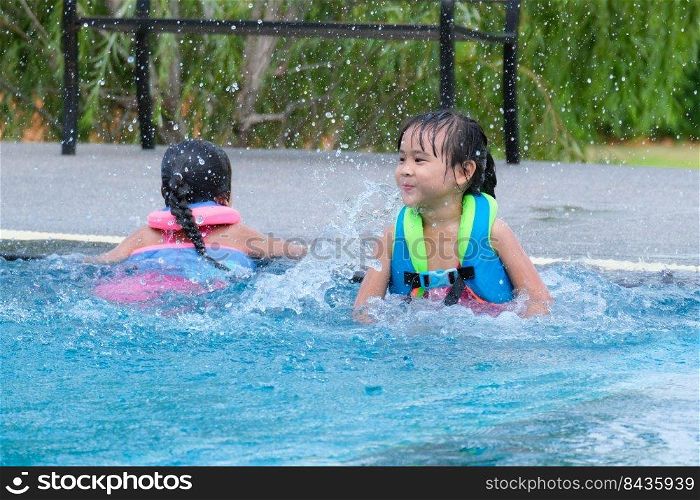 Little girl in a life vest jumps into an outdoor swimming pool. Cute little girl playing in the pool on a sunny day. Summer lifestyle concept.