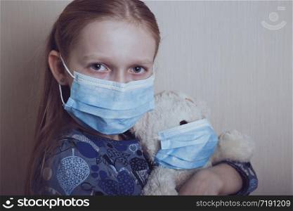 little girl in a medical mask holding a masked bear toy