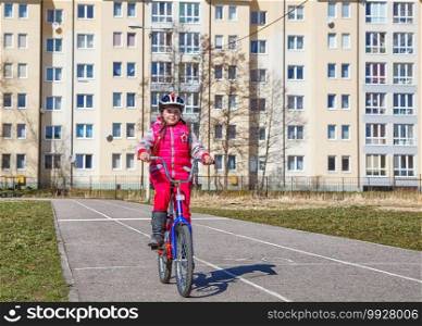 little girl in a red suit and a safety helmet riding a bicycle
