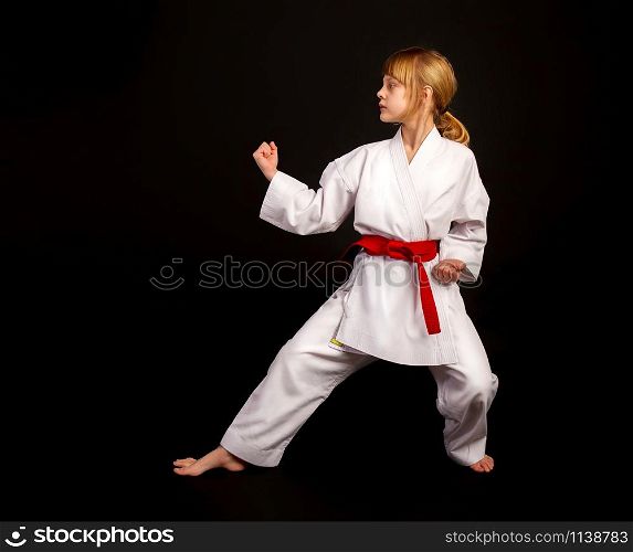 Little girl in a sports kimono and a red belt performs exercises in kata on a dark background. kata karate girl