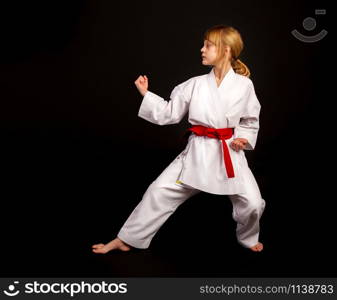 Little girl in a sports kimono and a red belt performs exercises in kata on a dark background. kata karate girl