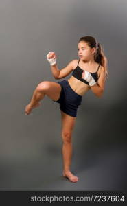 little girl in a sports tank top and shorts with hands wrapped in protective bandage is engaged in martial arts on a dark background. little mma girl