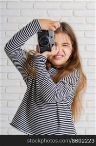 little girl in a striped blouse with a retro camera photographing standing near a light brick wall. girl with photocamera