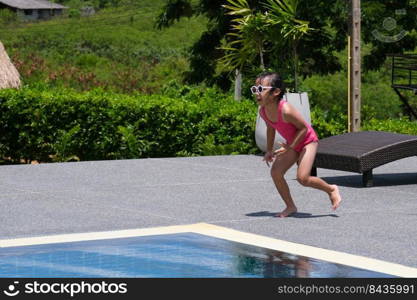 Little girl in a swimsuit and sunglasses runs by the pool on a sunny day. Little girls enjoy swimming in the pool. Summer lifestyle concept.