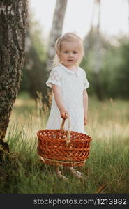 little girl in a white dress with a basket in the park. Beautiful baby girl walking in a sunny garden with a basket. Beautiful baby girl walking in a sunny garden with a basket. little girl in a white dress with a basket in the park