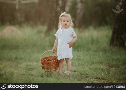 little girl in a white dress with a basket in the park. Beautiful baby girl walking in a sunny garden with a basket. Beautiful baby girl walking in a sunny garden with a basket. little girl in a white dress with a basket in the park