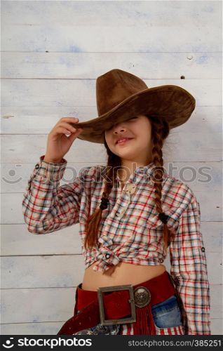 Little girl in a wide-brimmed cowboy hat and traditional dress posing on a light wooden background