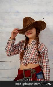 Little girl in a wide-brimmed cowboy hat and traditional dress posing on a light wooden background