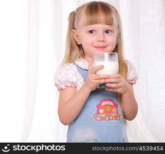 Little girl in blue dress drinks milk from a glass