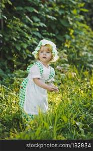 Little girl in green and white dress walking in the garden.. Girl in a dress in green peas in the garden 4652.