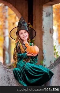 Little girl in halloween costume with jack pumpkin. Beautiful girl dressed as a witch in the park, outdoors.. Little girl in halloween costume with jack pumpkin. Happy halloween celebration.