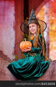 Little girl in halloween costume with jack pumpkin. Beautiful girl dressed as a witch in the park, outdoors.. Little girl in halloween costume with jack pumpkin. Happy halloween celebration.