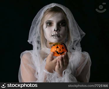 Little girl in Halloween ghost costume holding halloween pumpkin basket with worm candies, studio isolated on black background. Girl Halloween ghost with candy pumpkin