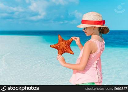 Little girl in hat with starfish on the tropical beach. Adorable little girl with starfish on white empty beach