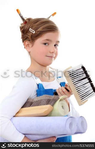 little girl in overalls holding painting materials