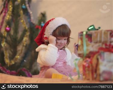 Little girl in red Santa hat near Christmas tree with gifts