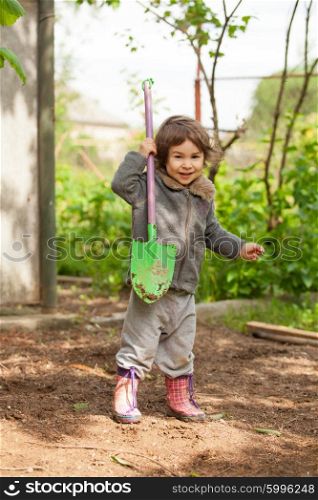 Little girl in rubber boots holding a shovel and tried to dig. The little girl with a small shovel