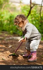 Little girl in rubber boots holding a shovel and tried to dig. The little girl with a small shovel