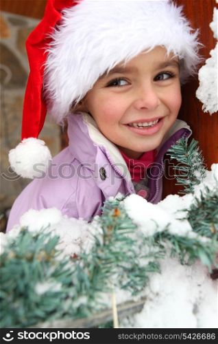 Little girl in Santa hat stood by tree