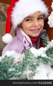 Little girl in Santa hat stood by tree
