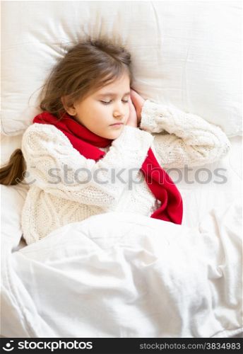 Little girl in sweater and scarf lying sleeping at bed