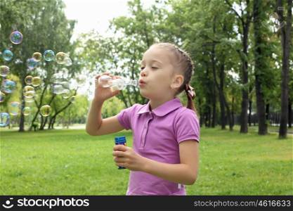 Little girl in the summer park blowing bubbles