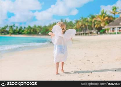 Little girl in white dress on the beach. Beautiful young girl wearing angel wings on the beach
