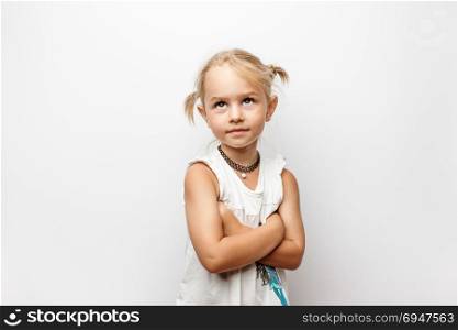 Little girl in white dress with crossed arms looks up on white background. Little girl in white dress with crossed arms looks up on white background.
