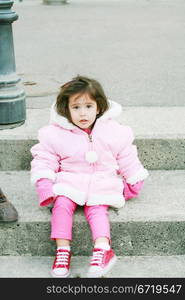 Little girl in winter clothes sitting in stairs looking at the camera.