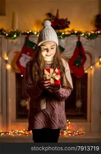 Little girl in wool sweater and hat looking inside of glowing present box