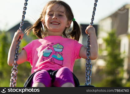 Little girl is all smiles on the swing at the park