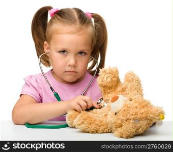 Little girl is examining her teddy bear using stethoscope, isolated over white