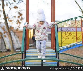 Little girl is playing on the playground in the park. The child goes on the steps of the playground.. Little girl is playing on the playground in the park. The child goes on the steps of the playground