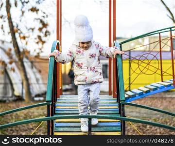 Little girl is playing on the playground in the park. The child goes on the steps of the playground.. Little girl is playing on the playground in the park. The child goes on the steps of the playground