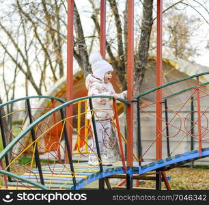 Little girl is playing on the playground in the park. The child goes on the steps of the playground.. Little girl is playing on the playground in the park. The child goes on the steps of the playground