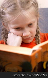 little girl is sitting in a chair and is reading a book