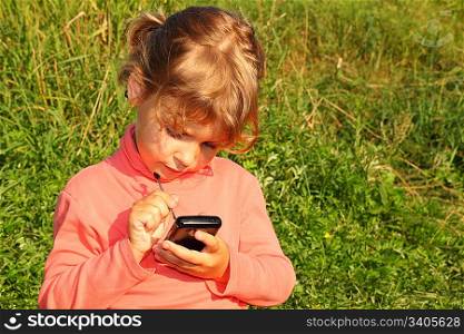 little girl is sitting on a grass of meadow with communicator.