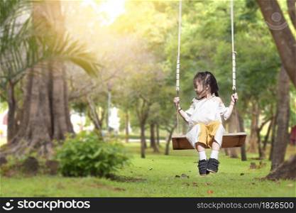 Little girl is swing at playground in summer garden on warm and sunny day outdoors.