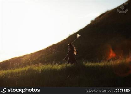 Little girl is walking with butterfly net and catching butterflies on the green hills on sunny summer day. copy space.. Little girl is walking with butterfly net and catching butterflies on the green hills on sunny summer day. copy space