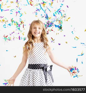 Little girl jumping and having fun celebrating birthday. Portrait of a child throws up multi-colored tinsel and confetti. Positive emotions. Happy excited laughing kid under sparkling confetti shower